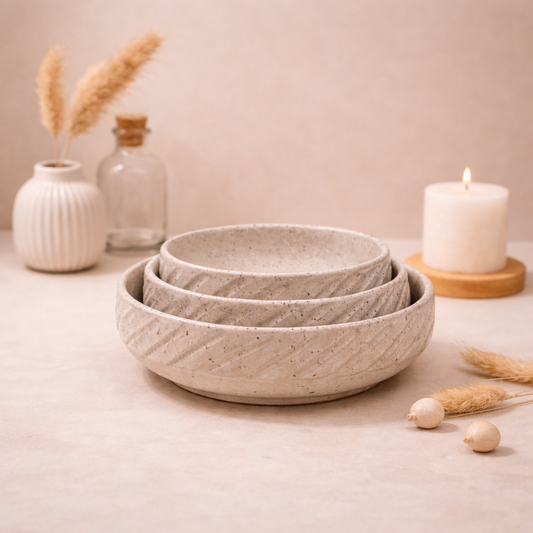 Set of three gray ceramic bowls on a light surface with decorative items.