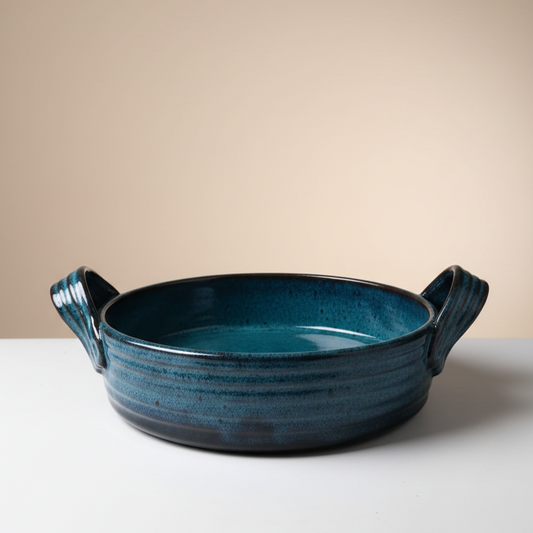 Blue ceramic bowl with handles on a white surface and beige background