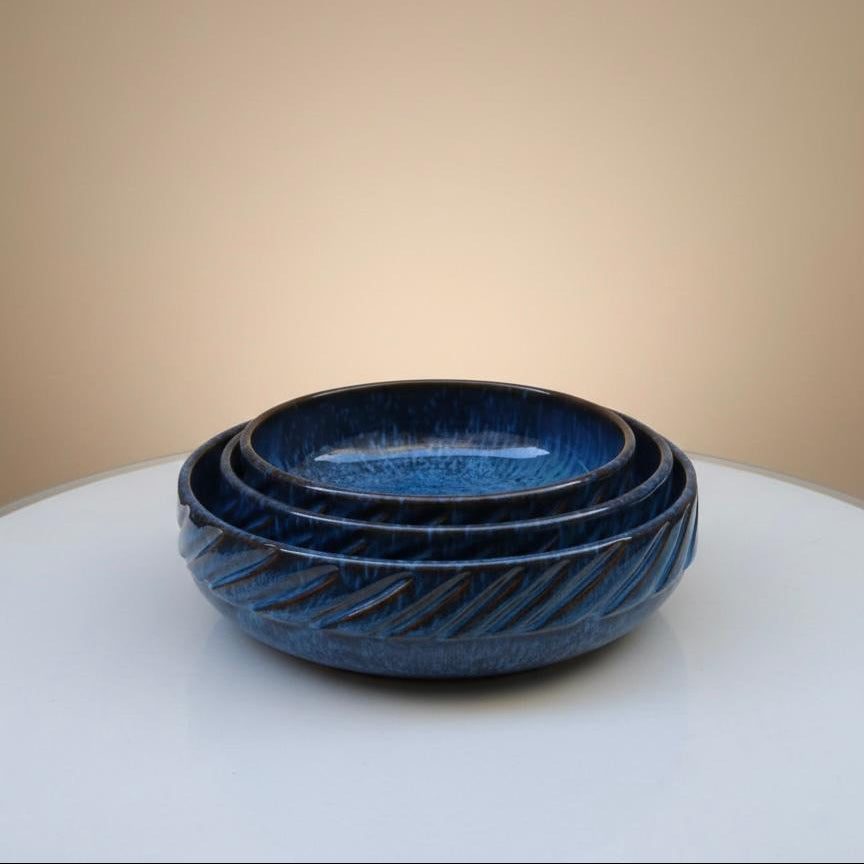 Set of three blue ceramic bowls on a white surface with a beige background